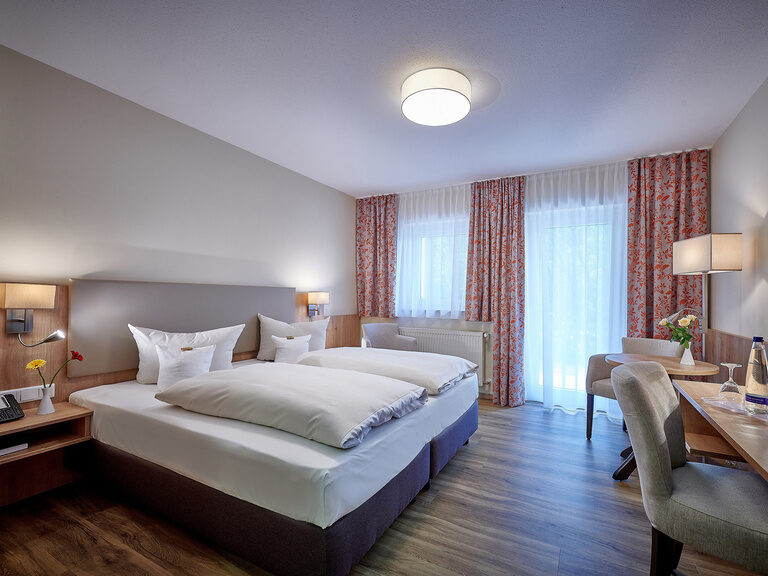 Das Doppelzimmer Ahorn beinhaltet unter anderem ein Doppelbett eine Fernseher einen Schreibtisch und Sessel